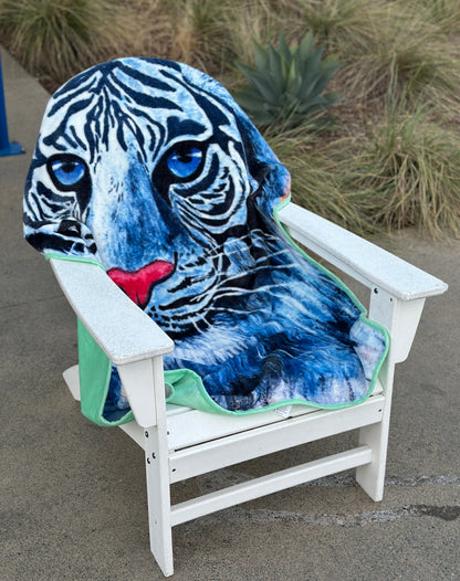 RTEM white tiger flannel throw blanket draped over a white chair outdoors, showing the blue-eyed white tiger illustration, soft fabric folds, and mint-green edging.