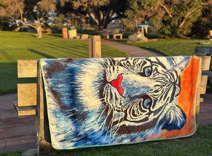 RTEM white tiger flannel throw blanket draped over a wooden park bench in warm afternoon sunlight, displaying the original blue-and-white tiger illustration against an orange background.