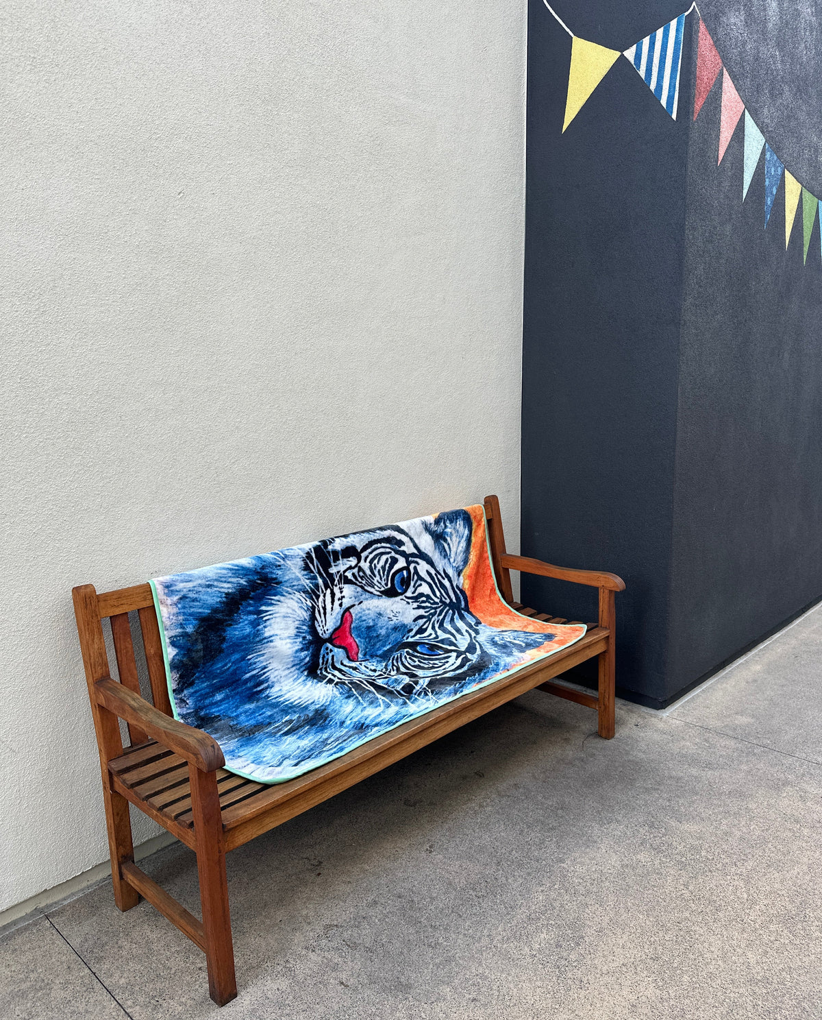 RTEM white tiger throw blanket spread across a wooden bench in an outdoor courtyard, featuring an original blue-and-white tiger illustration with vivid blue eyes and orange accents.